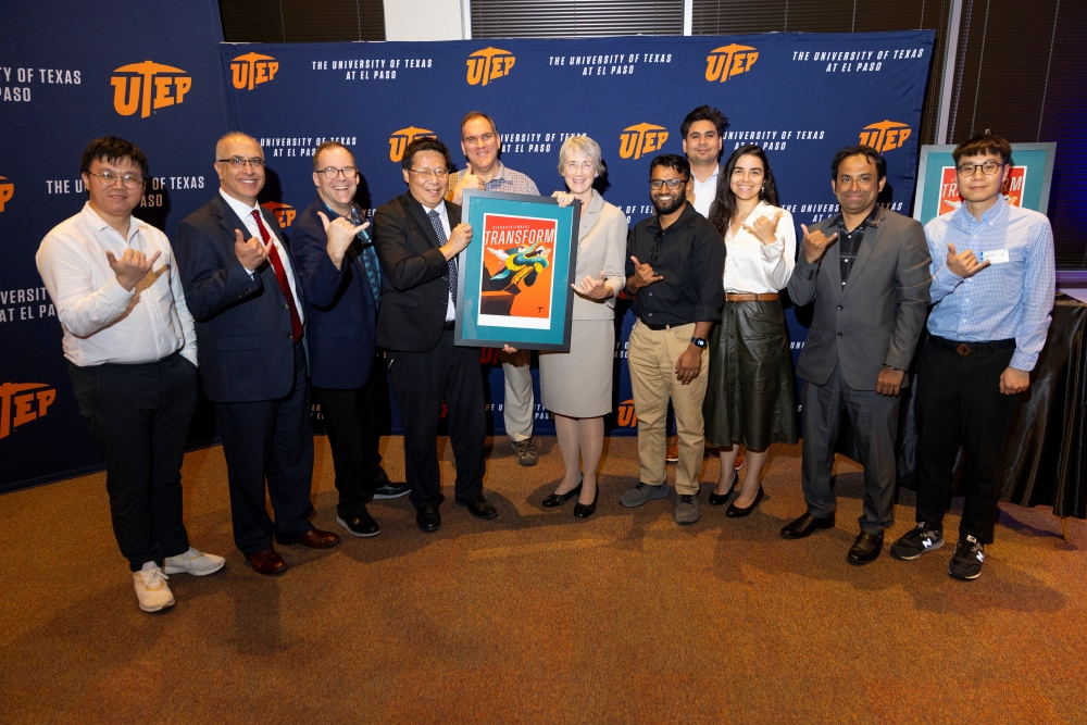 A large group poses with framed “Transform” artwork in front of a UTEP backdrop.